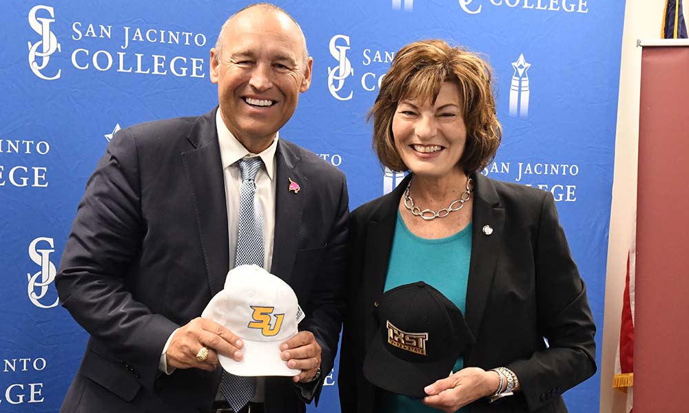 Dr. Kelly Damphousse, president of Texas State University and Dr. Brenda Hellyer, chancellor of San Jacinto College holding each college's hat and smiling for a photo.